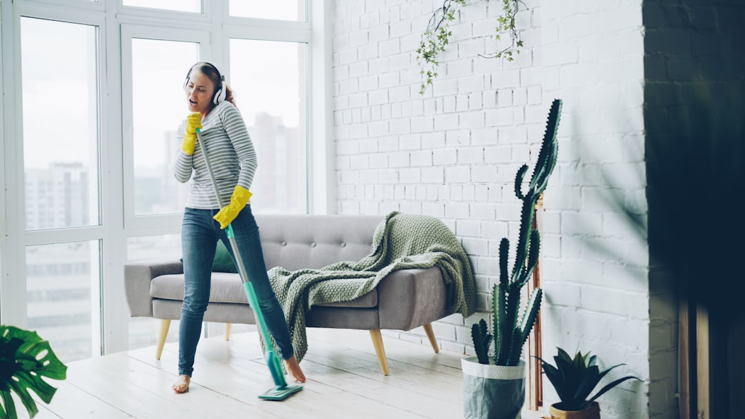 Happy young housewife is dancing and singing during housecleaning, she is listening to music in headphones and mopping floor having fun. Housework and technology concept.